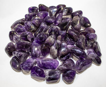 A collection of tumbled amethyst stones  with deep purple color of various sizes displayed on a white surface.